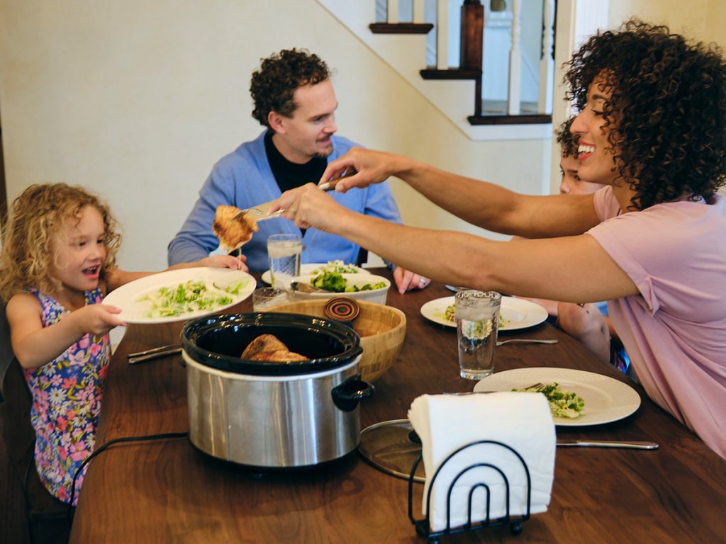Family eating together with a crockpot meal at dinner table.