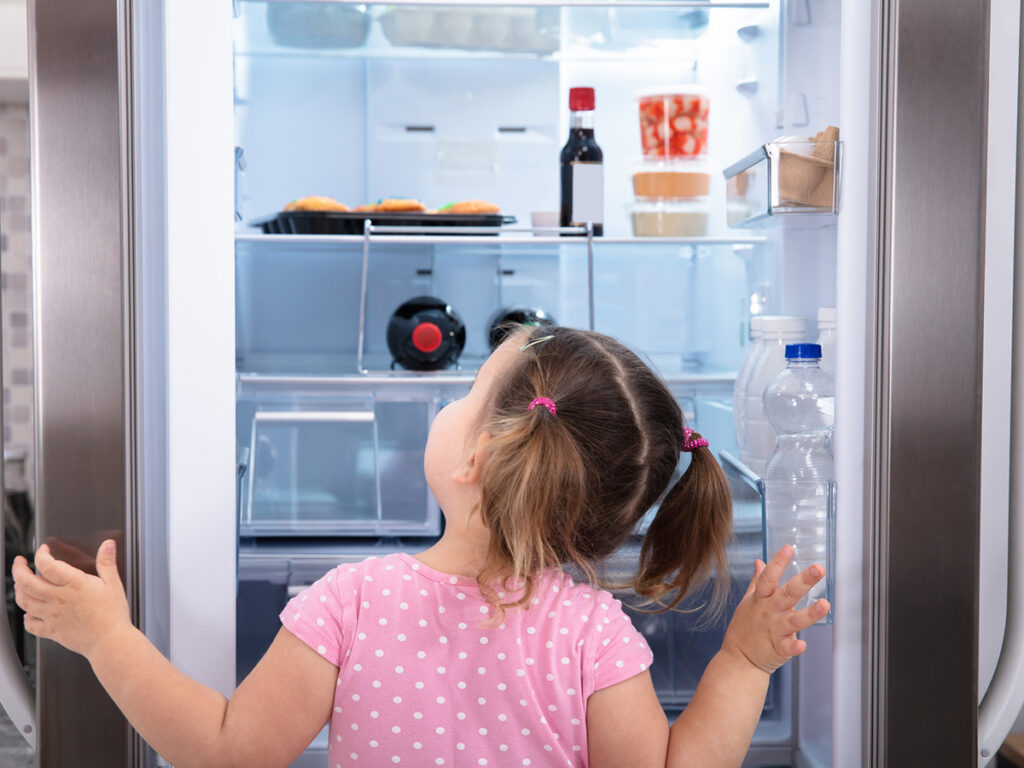 Little girl looking in refrigerator with little food in it